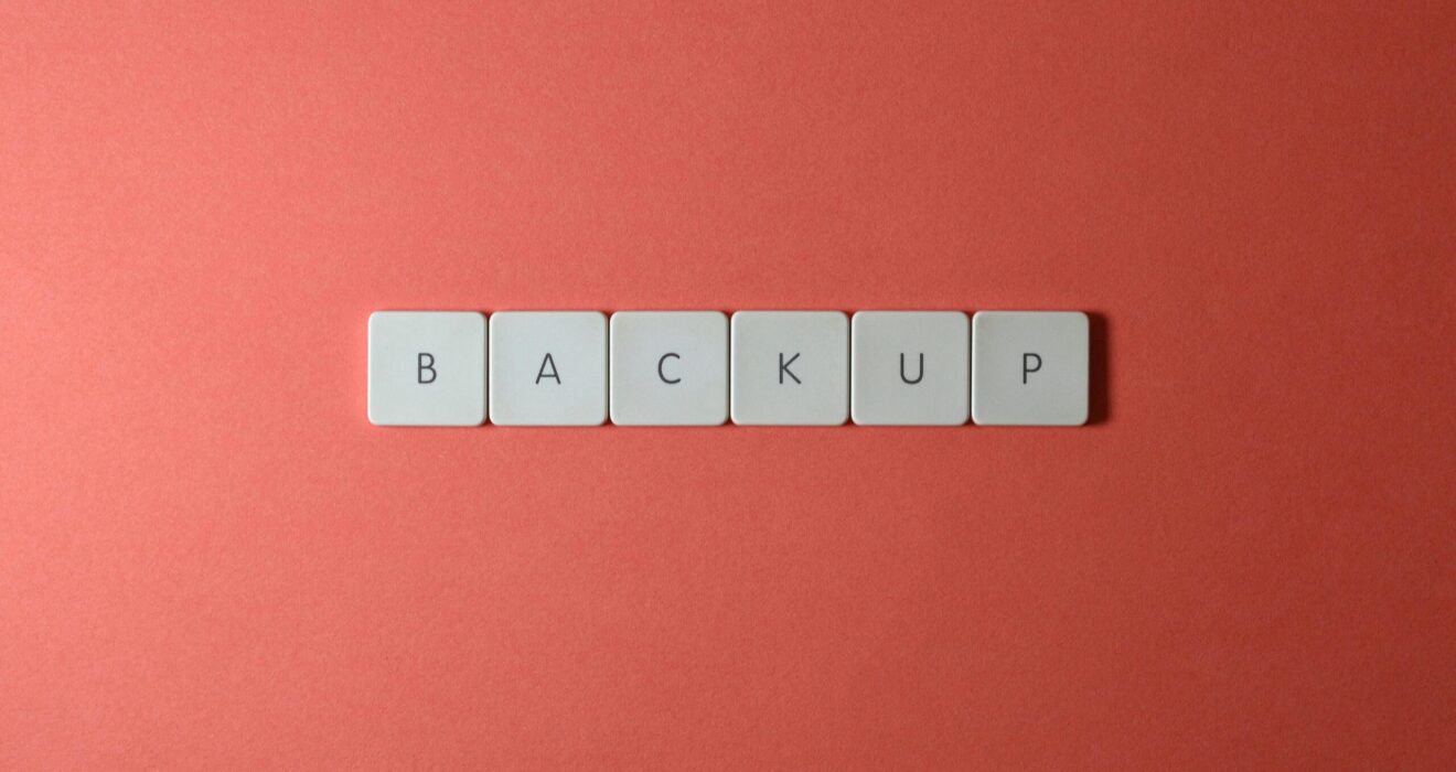 Free Close-up of keyboard keys spelling 'BACKUP' placed on a coral-colored surface. Stock Photo