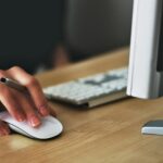 Free A hand using a wireless mouse at a modern desk setup with a computer and keyboard. Stock Photo