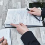 Free Close-up of hands analyzing insurance policy paperwork with pen on table. Stock Photo